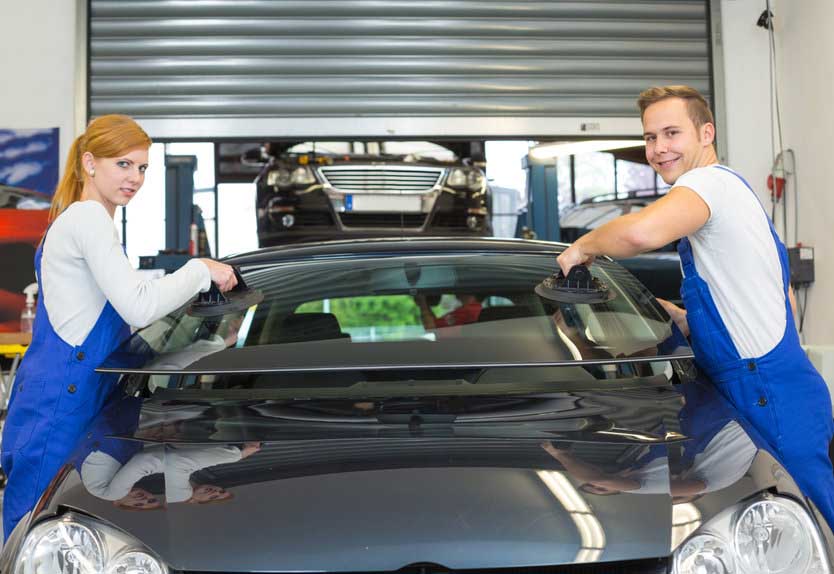 Two glaziers replace windshield or windscreen on a car in workshop after stone-chipping